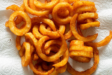 Seasoned spicy curly fries, freshly fried, on kitchen paper towel absorbing the grease. Fast food background backdrop.