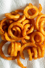 Seasoned spicy curly fries, freshly fried, on kitchen paper towel absorbing the grease. Fast food background backdrop.