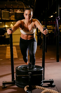 Attractive girl in the gym pushing metal sleds with weights