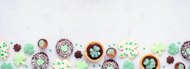 St Patricks Day dessert bottom border over a white stone banner background. Shamrock and green cookies, tarts, chocolate and candy. Top view. Copy space. © Jenifoto