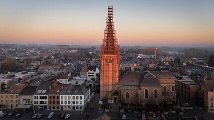 Obraz premium aerial view, drone view of the Sint-Servatiuskerk church in Diepenbeek, Belgium. The tower is standing in construction scaffolding for renovation of the tower. Early morning sunrise during winter.