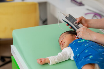 Pediatrician examining newborn baby's hearing with medical device
