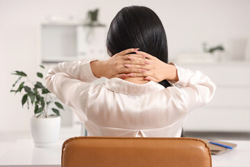 Beautiful young Asian businesswoman suffering from back pain on chair in office, back view