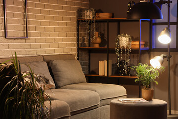 Cozy sofa, coffee table and glowing lamps in interior of living room at evening