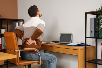 Young man suffering from back pain at table in office