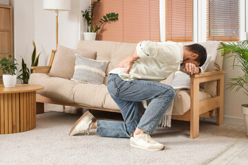 Young man suffering from back pain near sofa at home