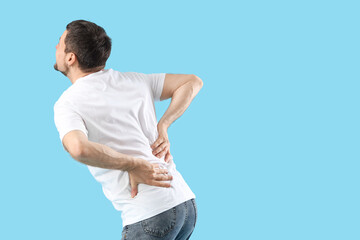 Young man suffering from back pain on blue background