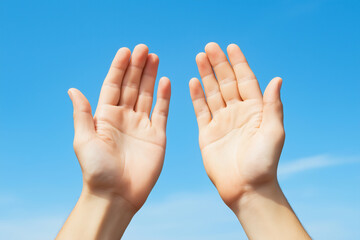 Hands reaching towards a clear blue sky on a sunny day with soft clouds