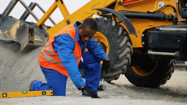 African American construction worker laying paving stones near excavator