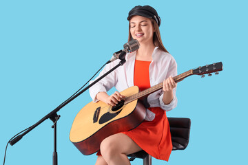 Young woman with microphone and guitar singing on blue background
