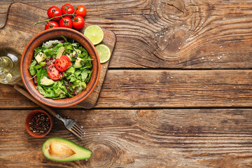 Bowl of tasty avocado salad with cherry tomatoes and lime on wooden background