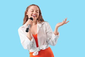 Beautiful young woman with microphone singing karaoke on blue background
