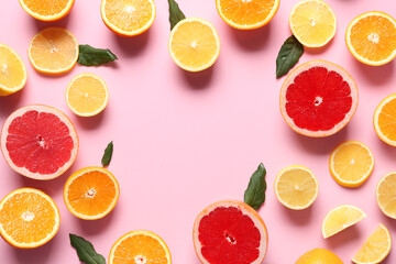 Frame made of different cut citrus fruits and leaves on pink background