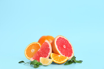 Different cut citrus fruits with mint leaves on blue background