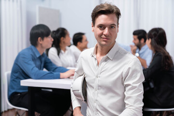 Confidence and happy smiling businessman portrait with background of his colleague and business team working in office. Office worker teamwork and positive workplace concept. Prudent