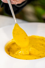 A close-up of a spoon lifting creamy yellow sauce from a white plate. The vibrant sauce has a...