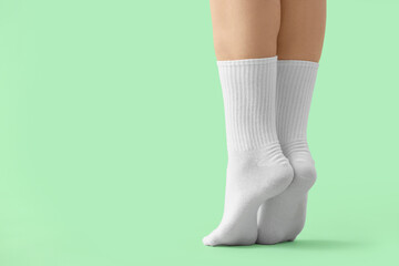 Legs of young woman in stylish white socks on green background