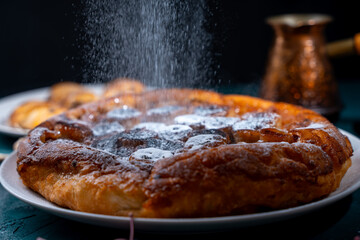 Banana Tarte Tatin is sprinkled with powdered sugar on a white plate on a dark background. The powder is poured onto the cake. Vertical Photo