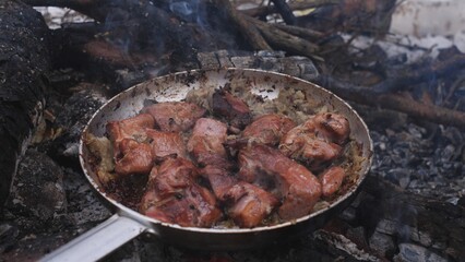 Sizzling, juicy meat is cooking over a roaring open flame in a large frying pan