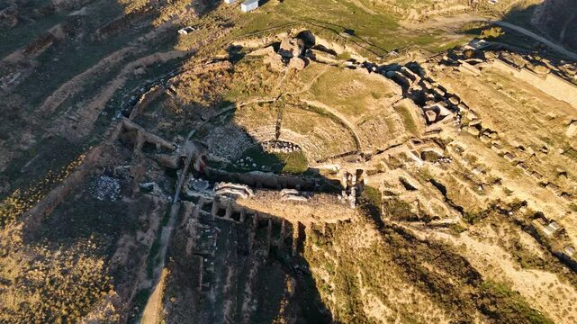 Aerial view of an ancient amphitheater of Augusta Bilbilis in northern Spainwith partially collapsed stone structures, surrounded by rugged terrain and pathways, captured during golden hour.
