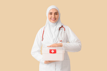 Female Muslim doctor in hijab with first aid kit on beige background