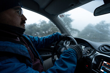 man driving very warm, with hat, jacket and gloves, winter atmosphere inside the car and scenery