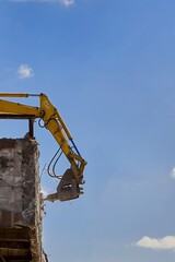 Excavator with a hydraulic breaker demolishing a concrete structure against a blue sky.