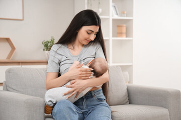 Young woman breastfeeding her baby while sitting on sofa in living room at home
