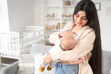 Young woman breastfeeding her baby in children's room at home
