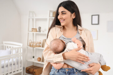 Happy young woman breastfeeding her baby in children's room at home