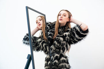 Fototapeta premium A fashionable woman poses in a black and white faux fur coat with a bold pattern, wearing a black lingerie-style top. Her long, straight, light brown hair and confident expression add to the chic, edg