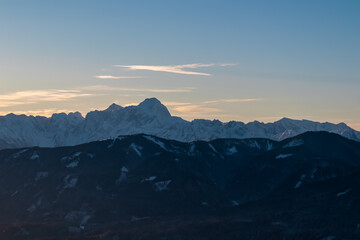 Scenic view of majestic snow-capped peaks of Julian Alps rising above forested mountains at sunset, viewed from Bad Bleiberg, Carinthia, Austria. Serene winter alpine landscape in remote Austrian Alps