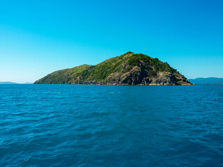 Naklejka premium Rugged mountainous island rising from crystal-clear turquoise waters in the Whitsundays archipelago, Queensland, Australia. Pristine natural beauty of the Coral Sea. Remote secluded island