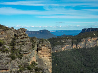 Dramatic sandstone cliffs and escarpments dominate the landscape at Blue Mountains National Park, Australia. Layered rock formations rise against a vibrant blue sky. eucalyptus forest below