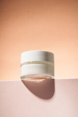 Cream jar on podium with beige background.