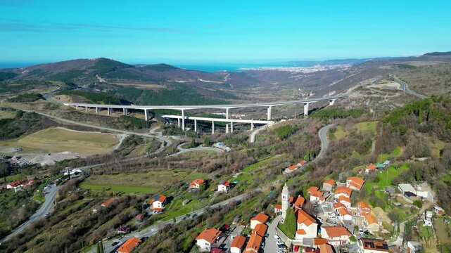 A stunning aerial drone view of Črni Kal, Slovenia, featuring the historic Castle of San Sergio atop a hill and the modern Črni Kal Viaduct, part of the A1 motorway (toll road), spanning Vipava Valley