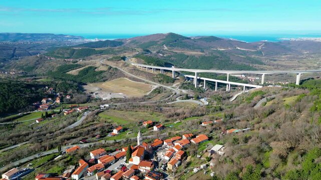 A stunning aerial drone view of Črni Kal, Slovenia, featuring the historic Castle of San Sergio atop a hill and the modern Črni Kal Viaduct, part of the A1 motorway (toll road), spanning Vipava Valley