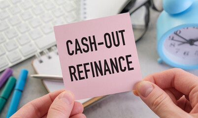 Cash-out refinance text on pink sticker in hands of businesswoman on office desk background