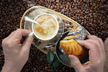 An elderly man holds a cup of espresso coffee in his hands. He adds sugar to taste and stirs it. Close-up of his hands.