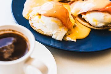 Egg Benedict with salmon and hollandaise sauce on a blue plate with a cup of freshly brewed coffee. selected focus. Concept: healthy breakfast