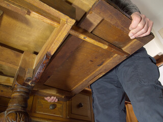 Closeup POV shot from underneath of a mid 20th century extending oak dining table, with a man’s...