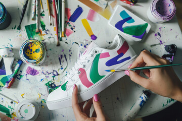close-up of an artist’s hands customizing white sneakers with vibrant abstract designs using a paintbrush and acrylic paints