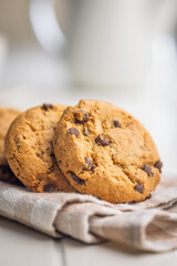 Chocolate chip cookies on napkin on white table.