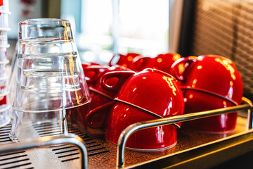 Many ceramic red coffee cups on a coffee machine shelf in a cafe. Selective focus. Red coffee cups on a shelf in a cafe, second row of selective red cup with soft focus.