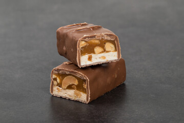 Candy bar. Nougat, caramel with peanuts, in milk chocolat. Dark background. Close up
