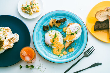 Poached eggs with hollandaise sauce on toast with crouton on a turquoise plate, next to a glass of orange juice and cutlery