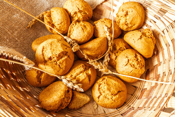 Freshly baked buns in a wicker basket with ears of wheat. Close-up. Selected focus.