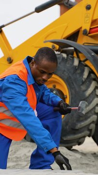 African American construction worker laying paving stones near excavator