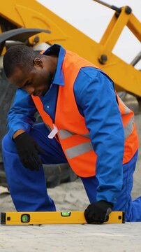 African American worker installing paving stones near heavy machinery
