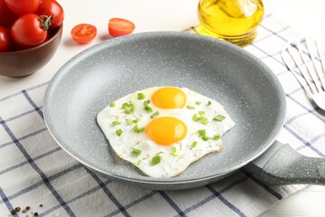 Tasty fried eggs with green onion in frying pan, oil and tomatoes on table, closeup